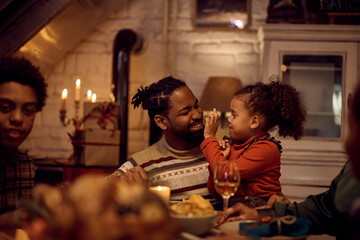 Obraz na płótnie Canvas Happy black father and daughter having fun during Thanksgiving lunch at dining table.