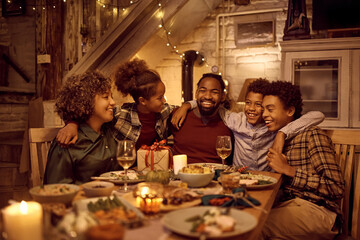 Happy multigeneration black family embracing during Thanksgiving meal at dining table.