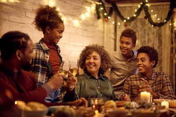 Happy black mature woman toasting with her family during Thanksgiving meal at dining table.