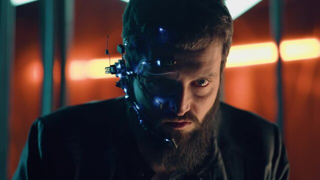 Brunette guy with dark beard wearing futuristic headset with one-eyed glasses, mic and ear piece looks at the camera with intense facial expressions. Neon lights in the background. Cyberpunk.