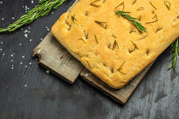 baked Italian homemade focaccia bread baking with rosemary and olive oil. Traditional Italian Focaccia on a dark background. banner, menu, recipe place for text, top view