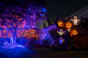 Night Halloween house outdoor decorations with glowing inflatable pumpkins and ghosts purple lights...