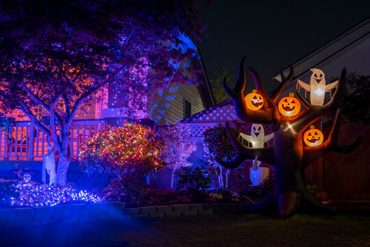 Night Halloween house outdoor decorations with glowing inflatable pumpkins and ghosts purple lights and orange garlands