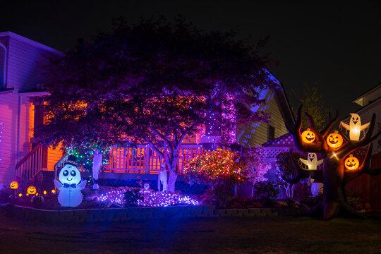 Illuminated night Halloween house outdoor decorations with colorful lights, pumpkins, lanterns, monsters and glow garlands