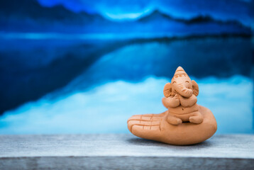 Elephant clay sculpture over blurred lake background, little cute Ganesh sculpture over blurred blue pattern background
