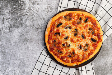 Homemade vegetarian pizza with mushrooms, cheese and tomato sauce on a round wooden cutting board on a dark grey background. Top view, flat lay