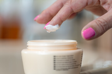 Senior woman's hand picking cream with her finger for personal skin care.