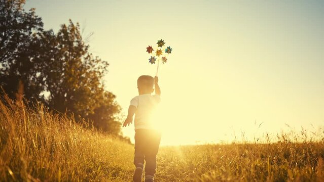 baby pinwheel. little boy silhouette plays with windmill a toy wind in the park. happy family childhood dream concept. boy play spinner toy glare of the sun at sunset in cheerful fun park