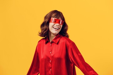 a stylish woman stands on a yellow background in a red shirt and glasses of an interesting shape smiling pleasantly at the camera