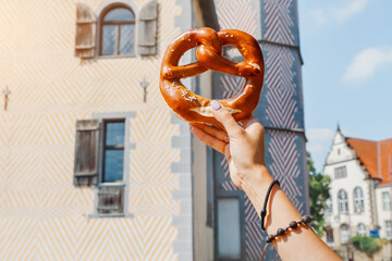female hand with german traditional pretzel on the background of an old German building. Travel and tourism
