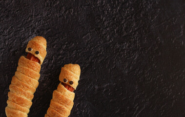 sausage in the dough in the form of a mummy on a dark background on the holiday halloween side arrangement