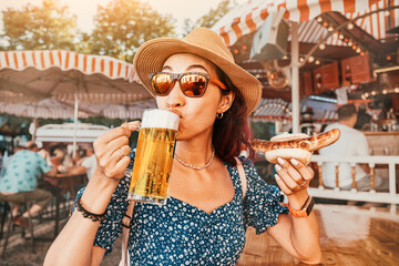 Happy girl drinking beer and eating traditional german bratwurst - hotdog at funfair and street...
