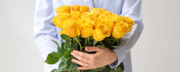 Young woman with bouquet of beautiful yellow roses on light background, closeup