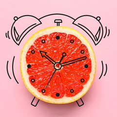 Fresh grapefruit and drawn alarm clock on pink background