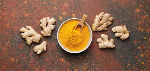 Bowl with turmeric powder and roots on grunge background