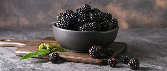 Bowl with tasty blackberries on grunge background
