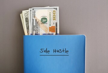 Cash dollar money in a blue notebook with text written on cover SIDE HUSTLE, on grey background, concept of making more money from side job with writing or freelance job