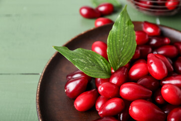 Plate with ripe red dogwood berries and leaves on color wooden table, closeup