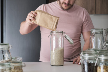 Unrecognizable latin man filling up a jar with basmati rice from a paper bag. Food in bulk delivery.