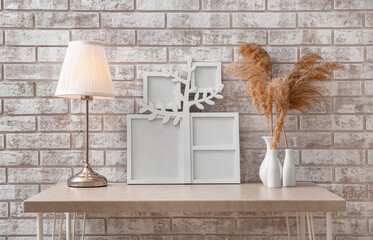 Family tree with photo frames, lamp and vases on table near light brick wall