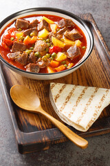 Orman Kebabı is a juicy meat dish that has plenty of peas and sliced potatoes closeup in the bowl on the table. Vertical