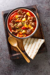 Fragrant lamb stew with carrots, potatoes, green peas and tomatoes close-up in a bowl on a wooden board. vertical top view from above