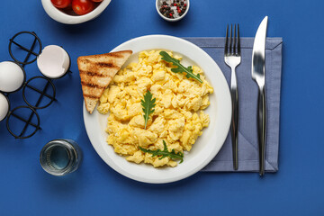 Composition with plate of tasty scrambled eggs and ingredients on blue background