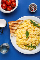 Composition with plate of tasty scrambled eggs and ingredients on blue background