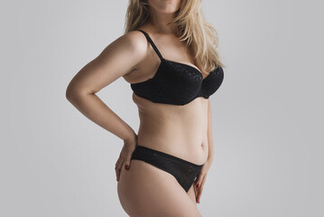 Young plus size woman with fat folds in black lingerie rear view on a gray background. The concept of body positivity and self acceptance. Unrecognizable figure of a woman with forms in underwear