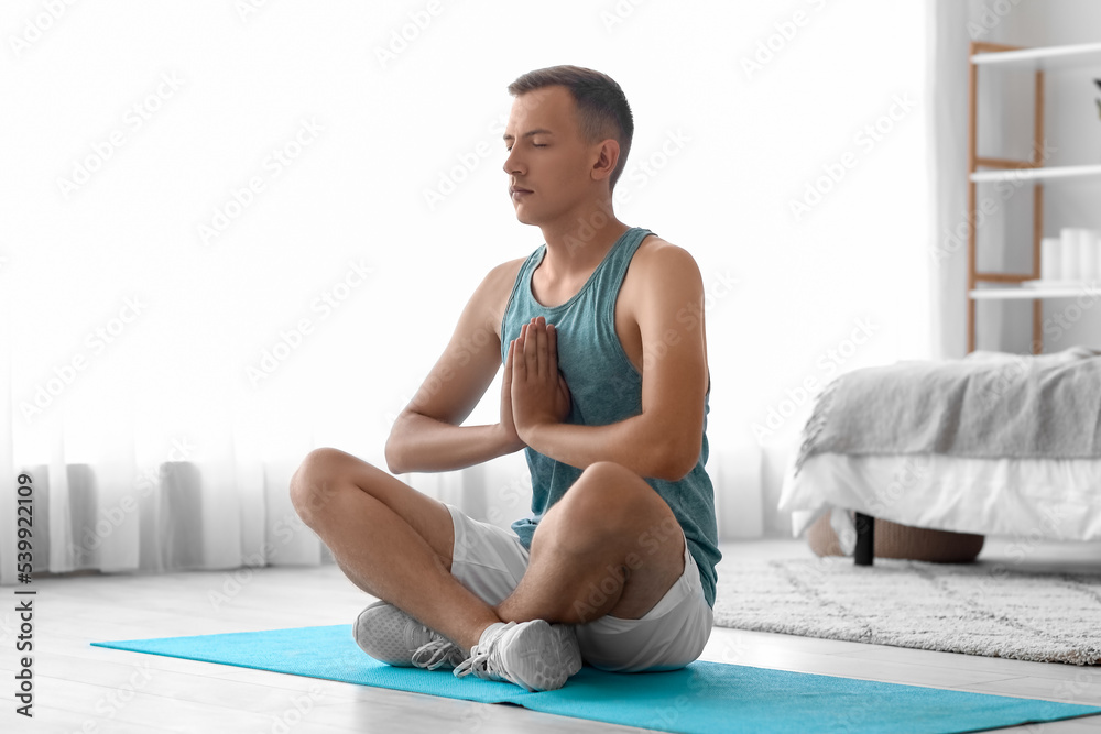 Poster Young man meditating on mat in bedroom