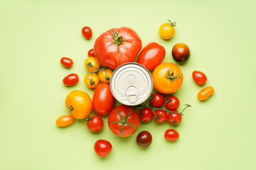 Tin can and fresh tomatoes on green background