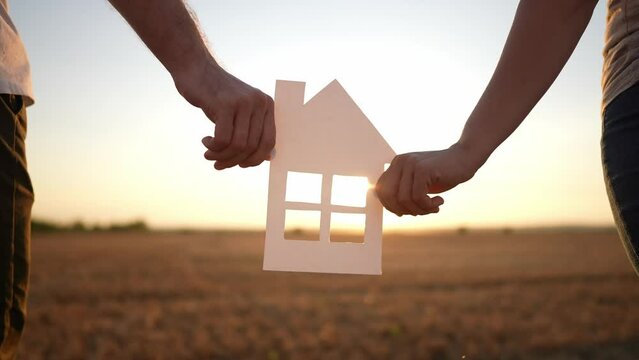 paper house happy family. friendly family hands holding paper house the glare of the sun shine through the window a beautiful sunset. mortgage lifestyle business construction concept. house dreams