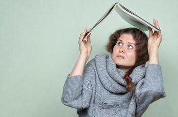 A woman hides under a book, as if under a roof from hostile factors: stress, depression, fear
