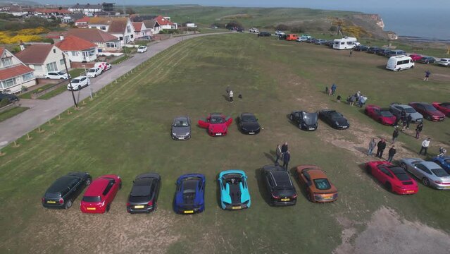 Aerial drone panning shot over rows of supercars parked outside Flamborough Head Lighthouse in Flamborough, UK at daytime.