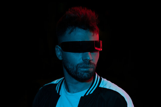 Model young man with beard in glasses of virtual reality on dark background. Augmented reality, future technology concept. VR. Blue neon light