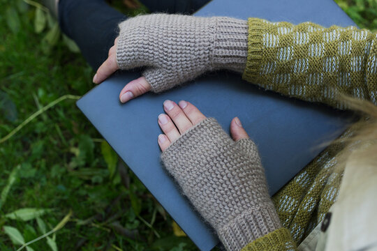
Female hands in warm woolen beige mitts on the laptop in the park. Woman working remotely outdoors, remote work concept.