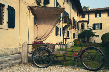 Vintage cargo tricycle loaded with red apples and flowers. Fall mood at Strassoldo village, Udine...