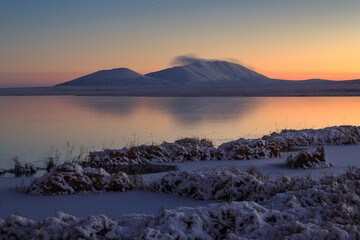 Beautiful evening arctic landscape. View of the mountain and the frozen lake in the snow-covered tundra. Cold autumn in the polar region. October in the Arctic. Frosty weather. Harsh northern nature.