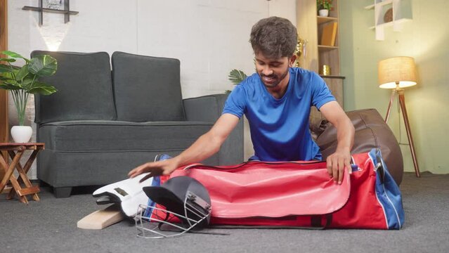 happy young cricketer packing his accessories kit for playing or practicing match at home - concept of sportsman, athlete and hobby or leisure activities