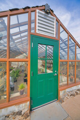 Fototapeta na wymiar Greenhouse exterior with green door below the stainless ventilation at Tucson, Arizona