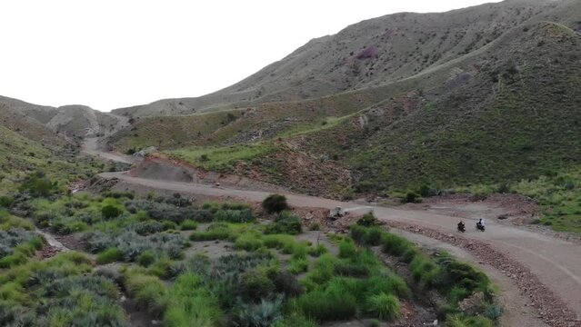 Aerial View Of Motorbikes Driving Along Remote Road Through Mountainous Valleys In Khuzdar. Tracking Shot