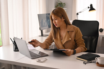 Professional businesswoman holding digital tablet and checking financial data on her laptop computer