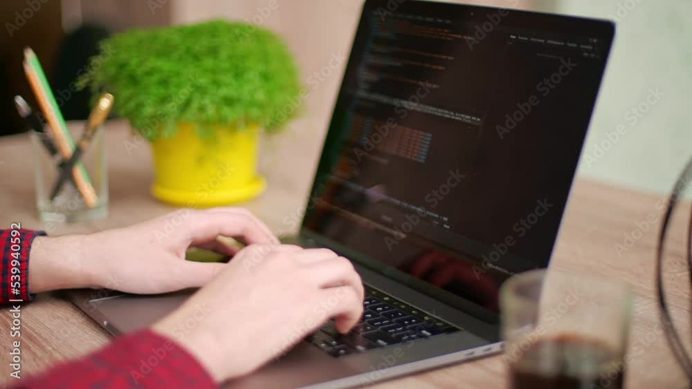 Wall mural close up of freelancer's hands typing code on laptop keyboard. camera slides around developer's fige