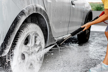 Close-up on woman holding high pressure pump washing her car in a self-service car wash station...