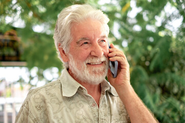 Portrait of attractive senior man standing in outdoor garden using mobile phone, elderly bearded grandfather relaxing enjoying tech and social