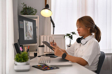 Creative woman using digital tablet, working on design project at graphic studio