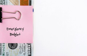 On white copy space background, cash dollar money clip with pink paper note EMERGENCY BUDGET, smart financial planning to save money for contingency fund - for rainy day, future crisis or distress