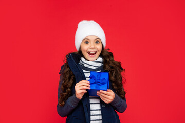 happy amazed child in puffer jacket and hat hold box. kid with present. teen girl