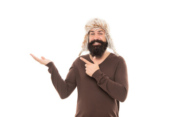 smiling mature guy with beard in earflape hat point finger on copy space, directing.