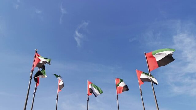 United Arab Emirates flags waving in wind in blue sky background. Seven UAE flags represent seven emirates.